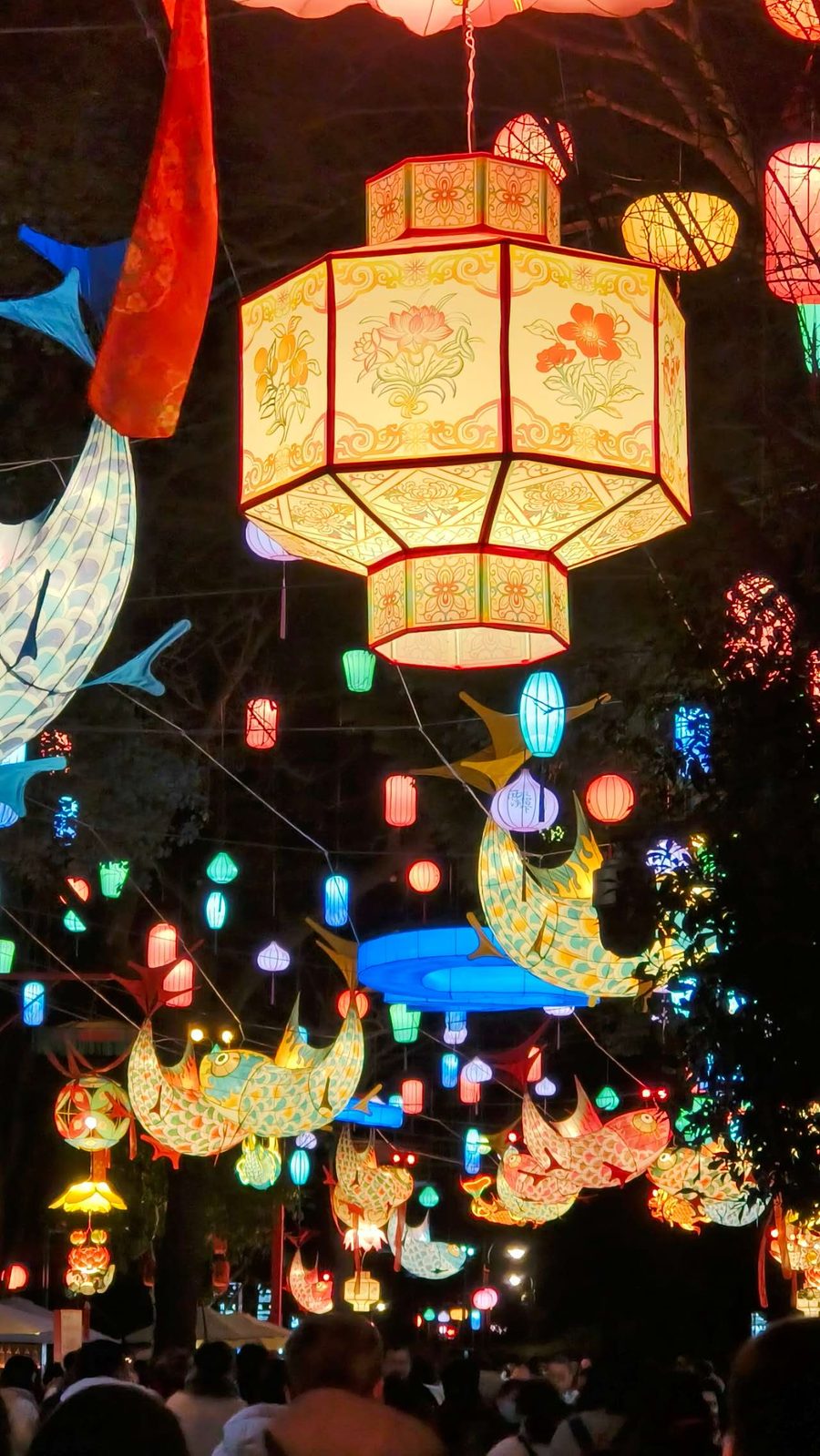 夜市灯会中高悬的八角花卉宫灯与游弋的彩色锦鲤灯
