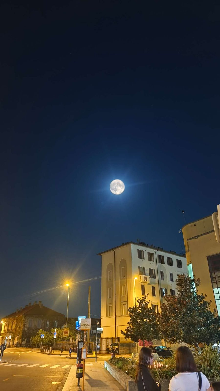 深蓝夜空中的一轮明月悬挂在街角楼房之上